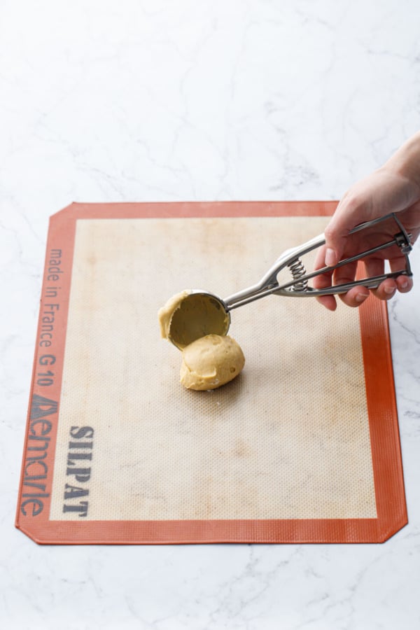 Cookie scoop dropping a dollop of batter onto a silicone baking mat.