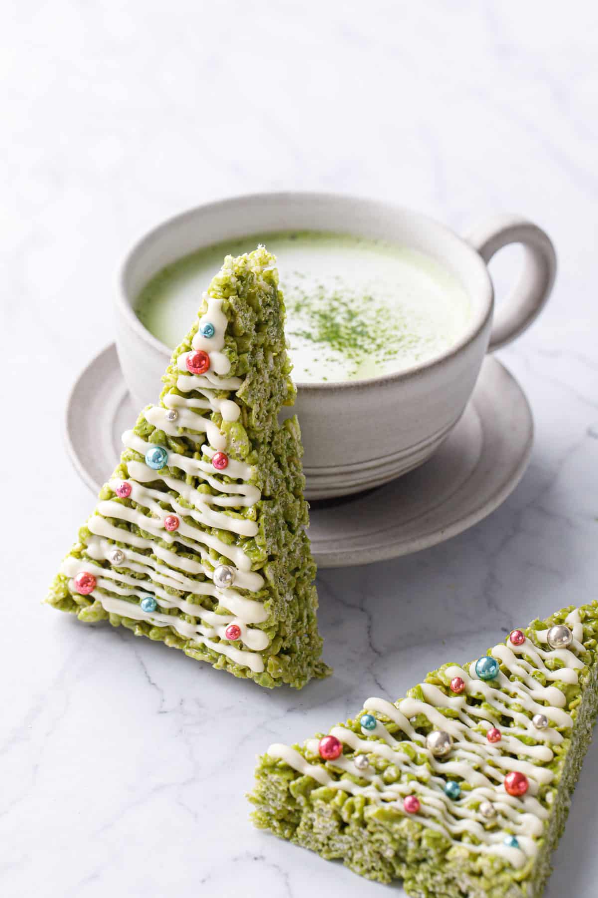 Matcha Rice Crispy Treats cut into a triangle and decorated like a Christmas tree, leaning up against a matcha latte.