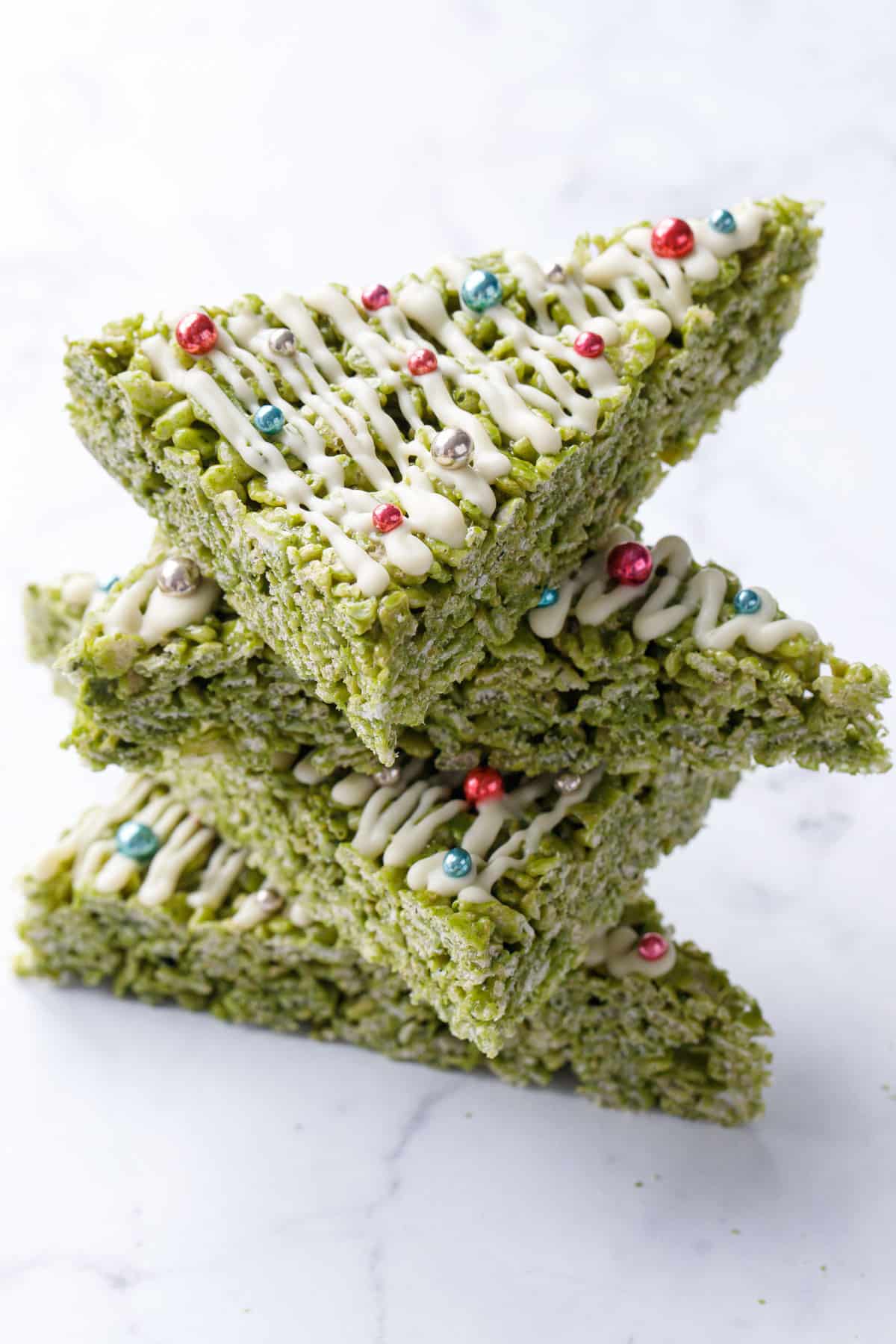 Stack of triangular Matcha Rice Crispy Treats decorated to look like Christmas trees on a marble background.