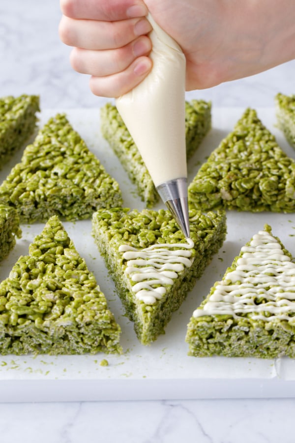 Piping bag drizzling white chocolate over Matcha Rice Crispy Treats.