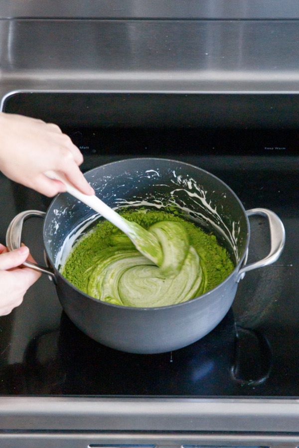 Stirring matcha powder into melted marshmallow mixture with a spatula.
