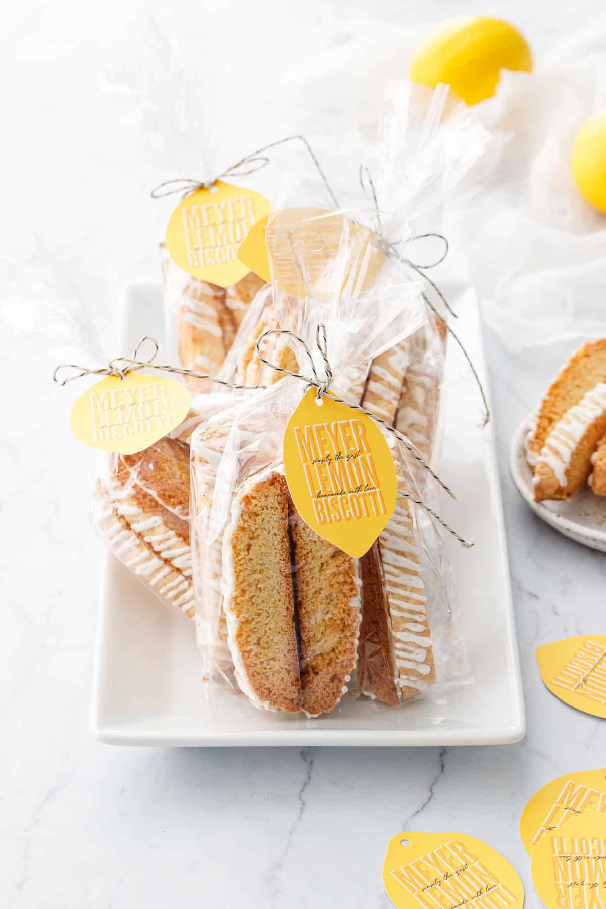 White plate with Meyer Lemon Biscotti in clear cello gift bags, tied with twine and a lemon-shaped gift tag.