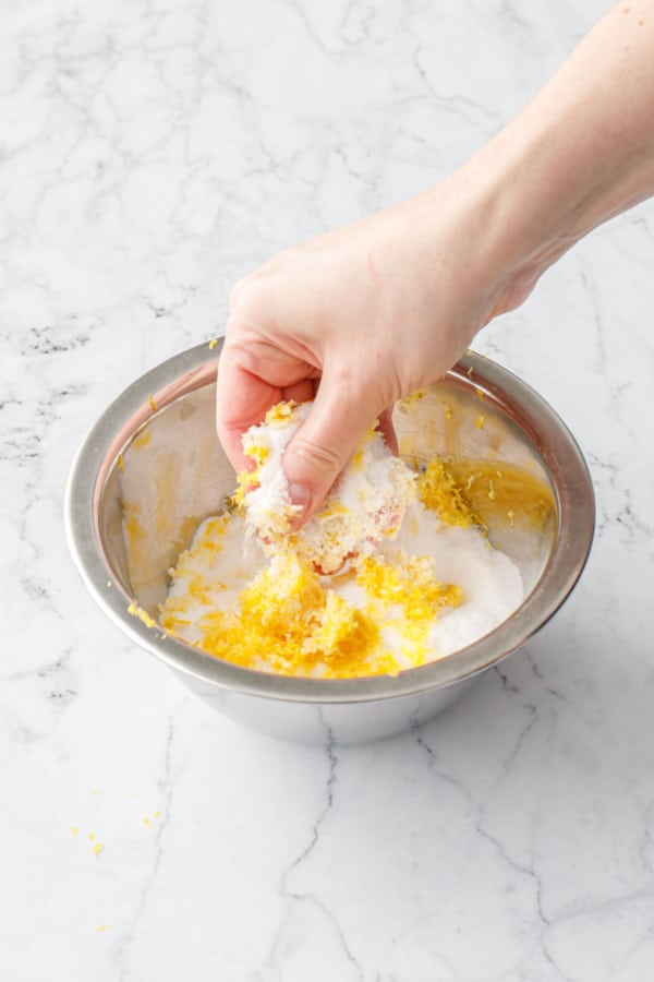 Rubbing lemon zest with granulated sugar with fingers in a small metal bowl.