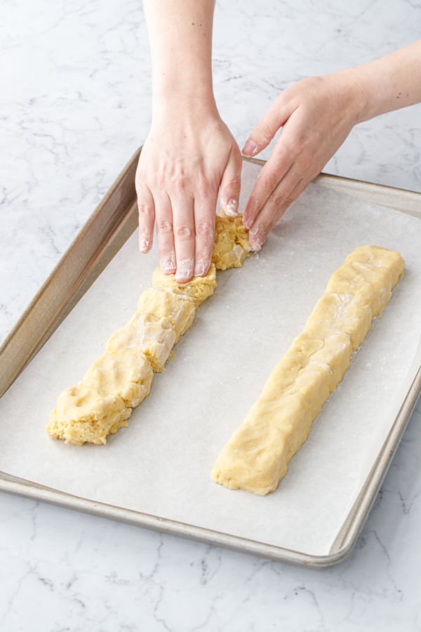 Lightly floured hands shaping the biscotti dough into two long logs.