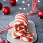 Red and white striped cake roll with chocolate peppermint whipped cream filling, with candy canes, red ornaments, and Christmas lights out of focus in the background.