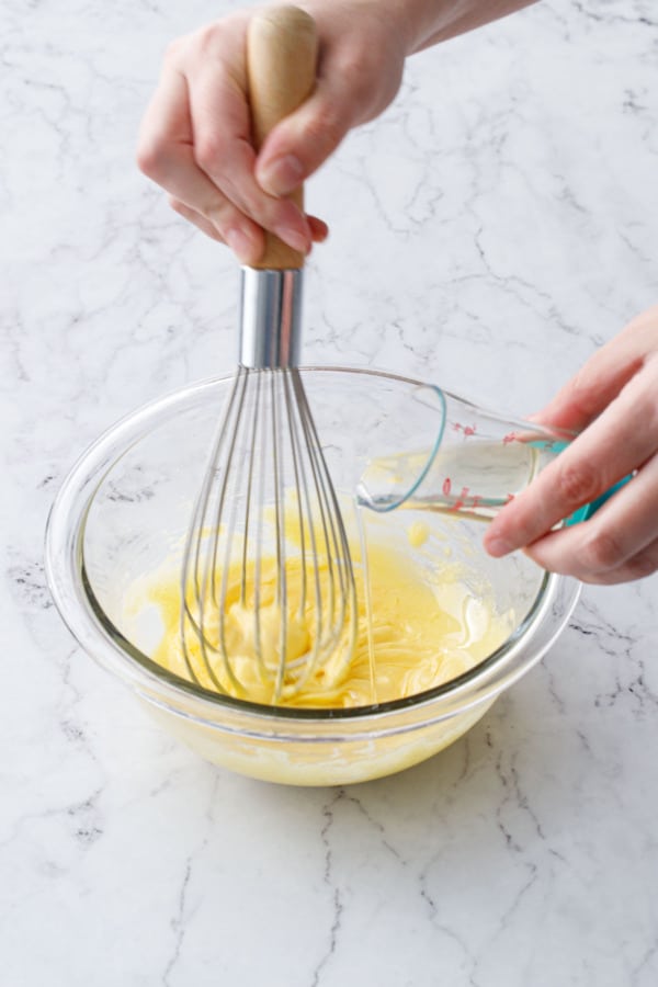 Drizzling oil from a beaker measurer into a mixing bowl while whisking.