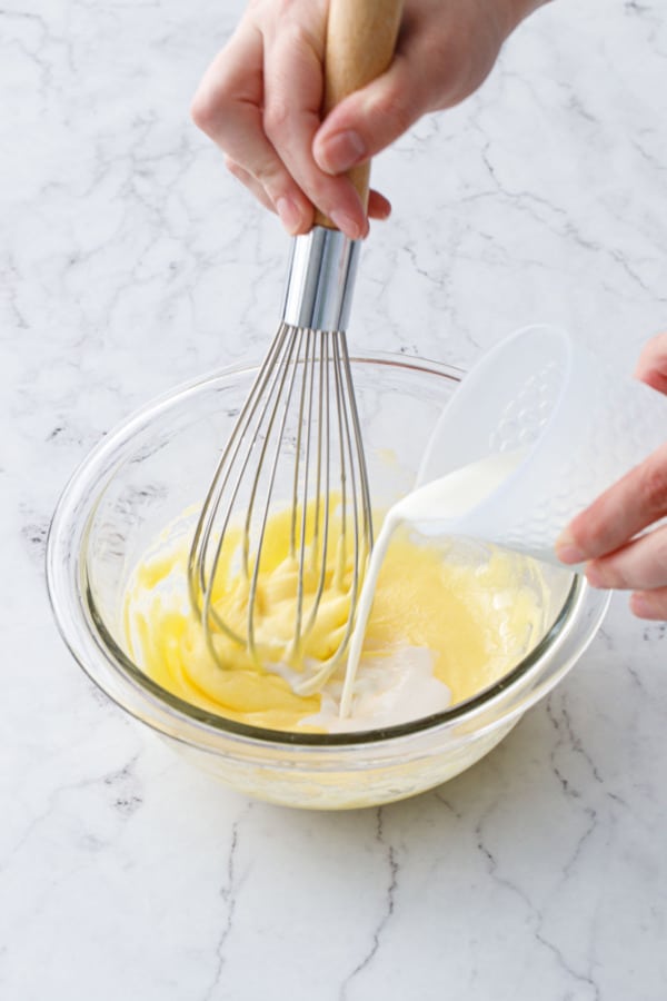 Pouring milk into a mixing bowl while whisking.