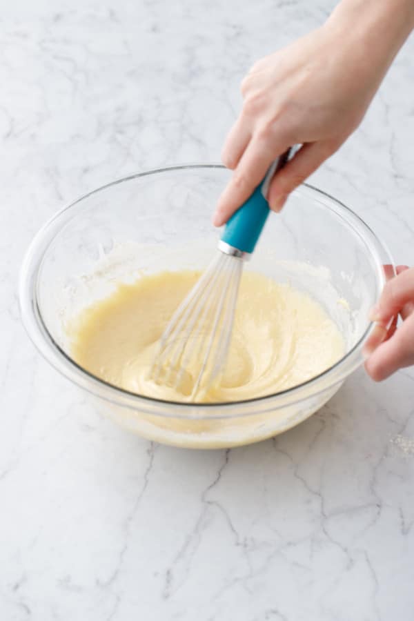 Whisking dry ingredients into wet ingredients in a mixing bowl until smooth.