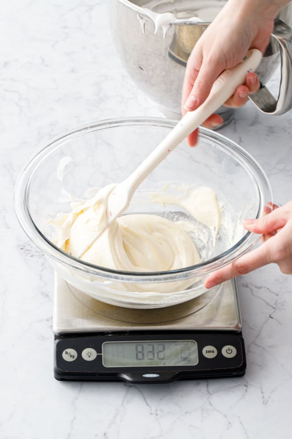 Spatula folding in the first addition of egg whites into the mixing bowl with cake batter sitting on a scale.