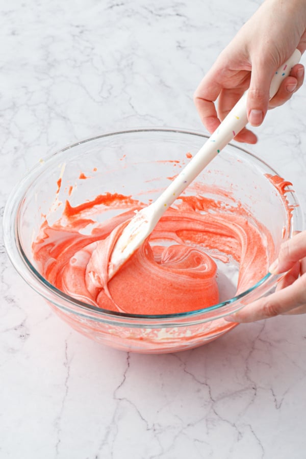 Folding egg whites into mixing bowl with red cake batter, which more clearly shows the whites being evenly incorporated.