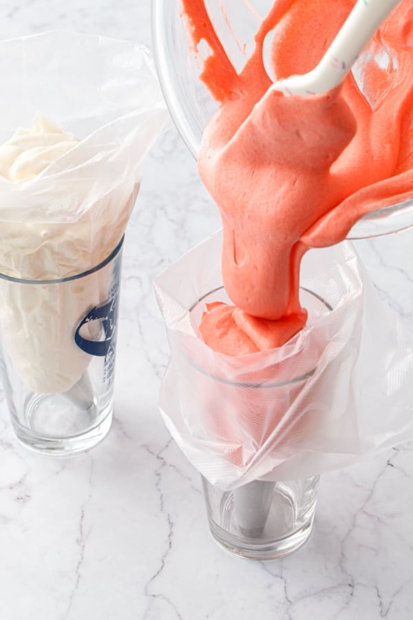 Pouring red cake batter into a plastic piping bag sitting inside a drinking glass to hold it upright.
