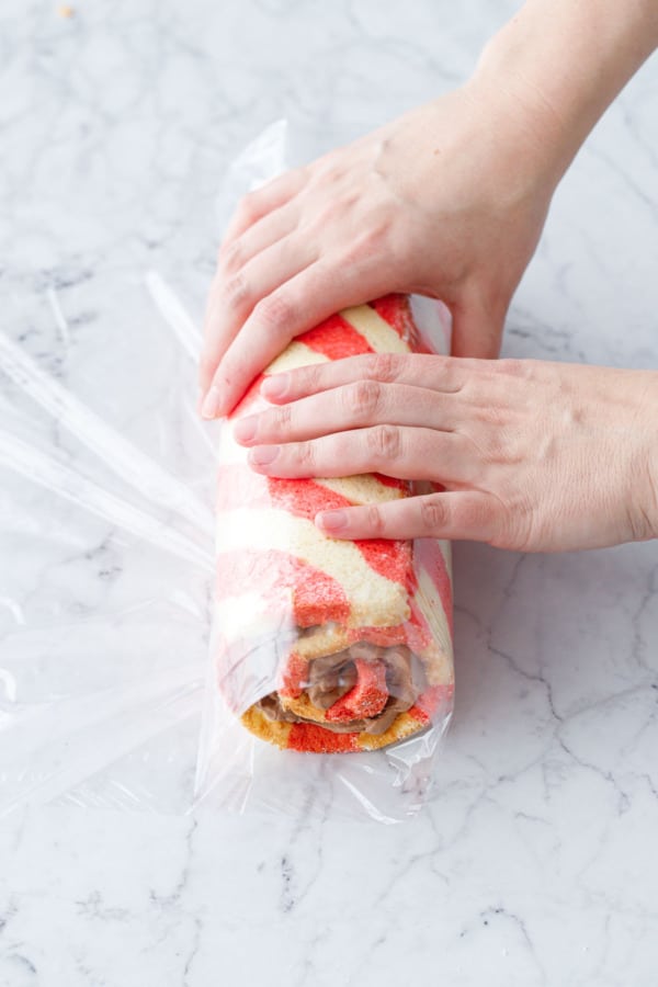 Wrapping the filled and rolled cake in clear plastic wrap.