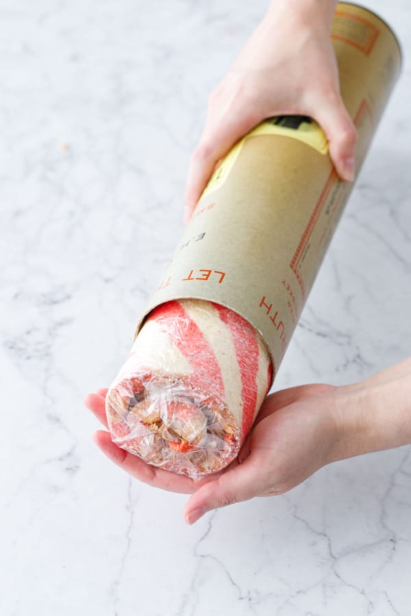 Placing the rolled and plastic-wrapped cake roll in a cardboard tube to preserve the shape.