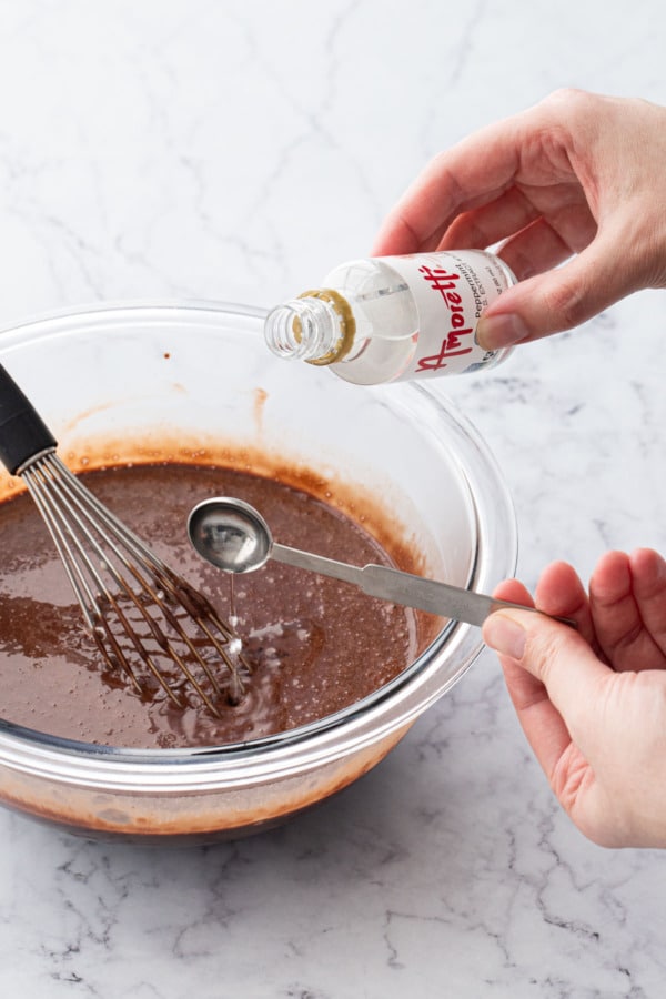 Measuring 1/2 teaspoon of peppermint extract and pouring into bowl with chocolate mixture and whisk.