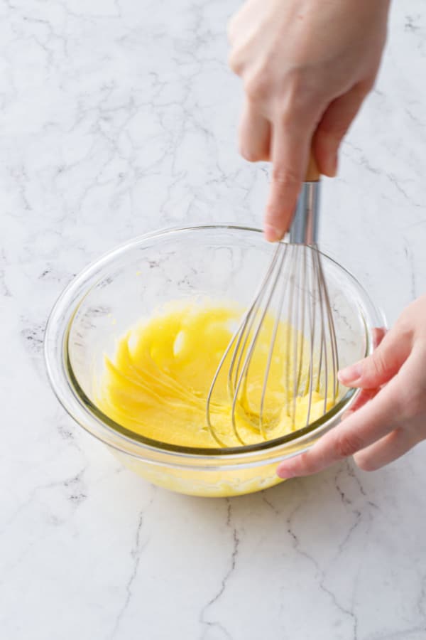 Small glass mixing bowl whisking together egg yolks and sugar until lightened in color.