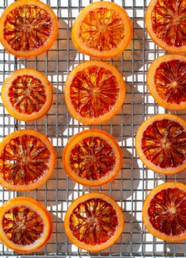 Homemade Candied Blood Orange Slices on a wire rack in bright direct light to showcase the stained-glass like appearance.