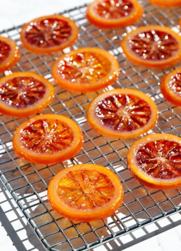 Homemade Candied Blood Orange Slices on a wire rack in bright direct light to showcase the stained-glass like appearance.