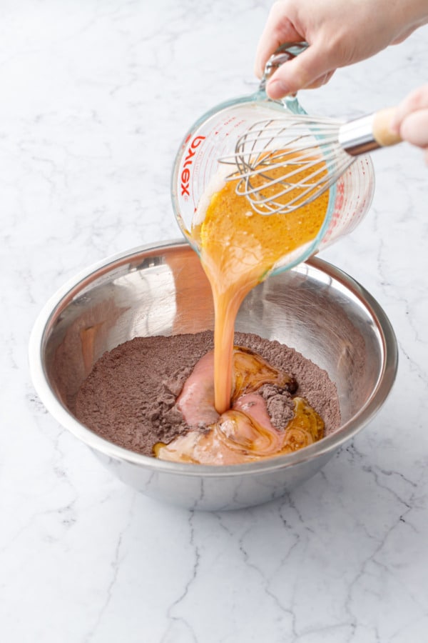 Pouring wet ingredients into mixing bowl with dry ingredients.