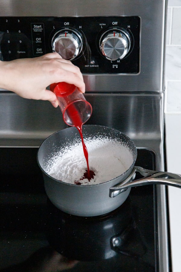 Pouring blood orange juice in to a small saucepan with sifted powdered sugar.