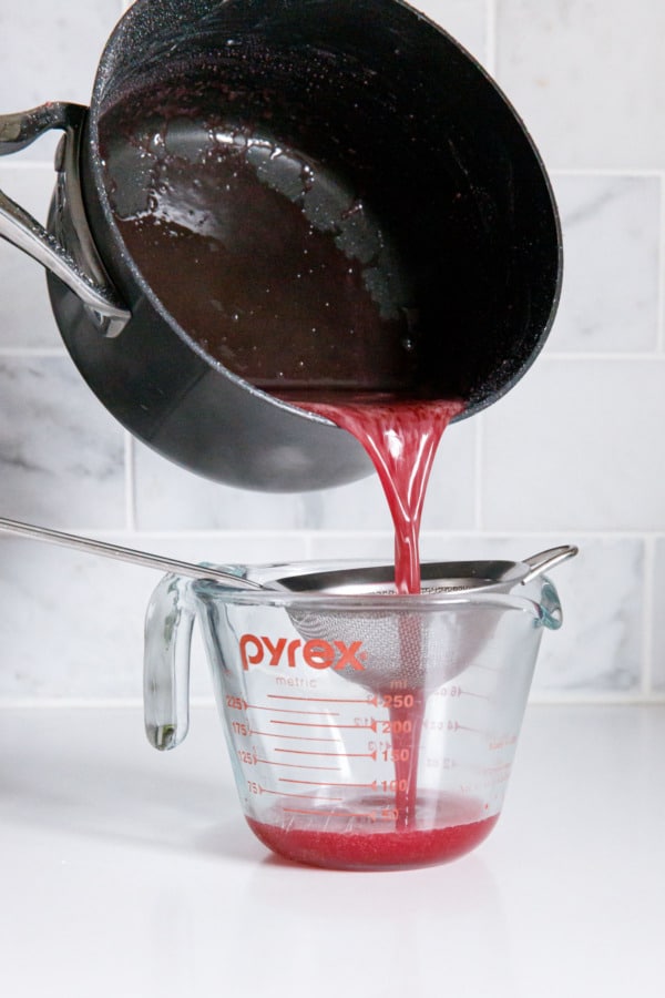 Straining blood orange sugar syrup through a small sieve into a glass measuring cup.