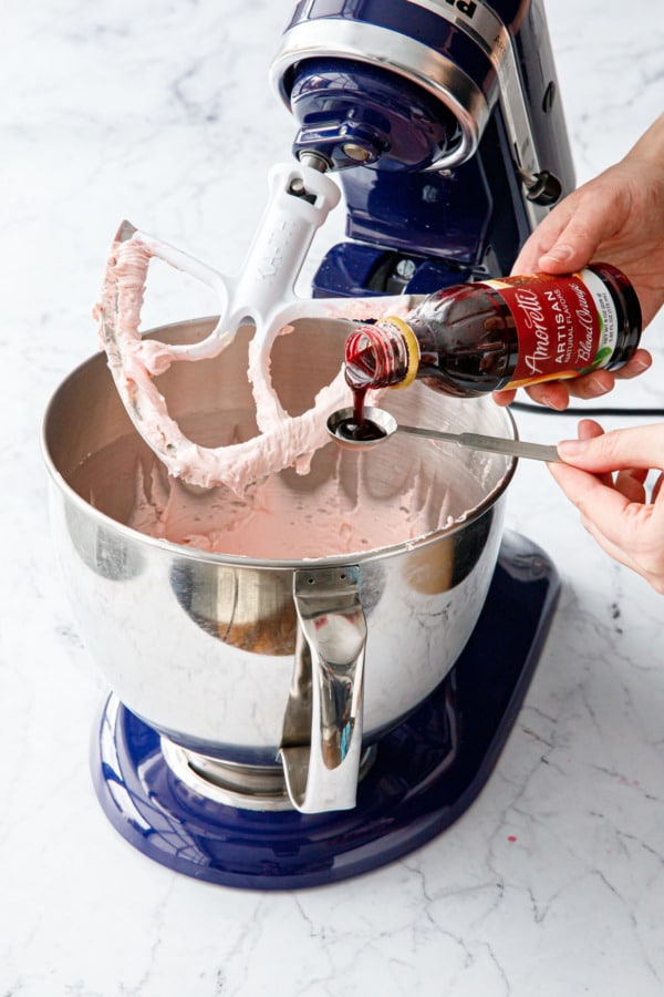 Measuring a teaspoon of Amoretti Natural Blood Orange Artisan Flavor into frosting in stand mixer.
