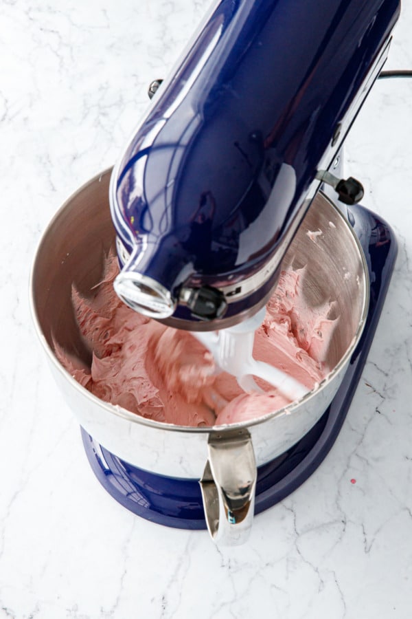 Looking down into the bowl of a stand mixer with fluffy blood orange frosting being whipped.