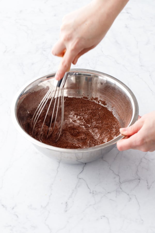 Whisking cocoa powder into dry ingredients in a stainless mixing bowl.