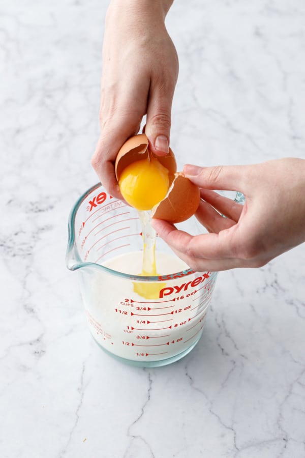 Cracking an egg into a 2-cup pyrex measuring cup with milk.