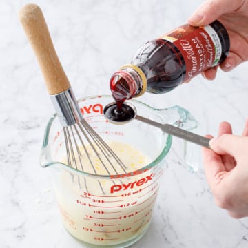Measuring a teaspoon of Amoretti Natural Blood Orange Artisan Flavor above a measuring cup with other wet ingredients.