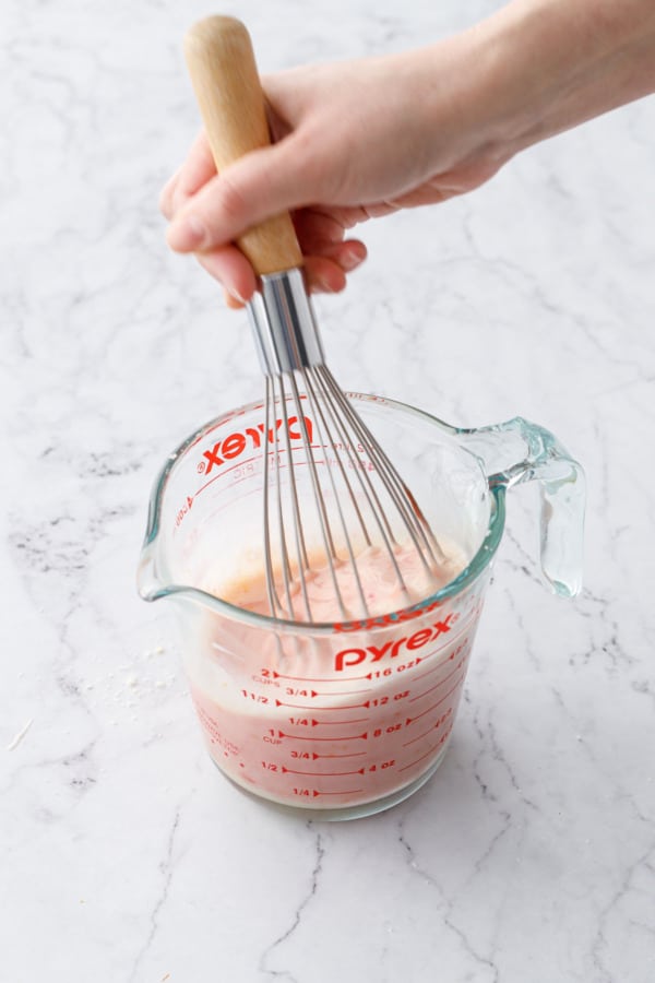 Whisking in blood orange flavoring, turning the mixture in the measuring cup light pink.