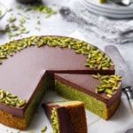 Flourless Pistachio Cake with Chocolate Ganache on a gray background, two slices cut to show the bright green color inside.