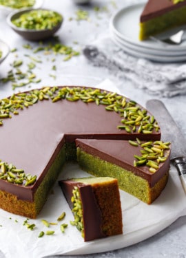 Flourless Pistachio Cake with Chocolate Ganache on a gray background, two slices cut to show the bright green color inside.