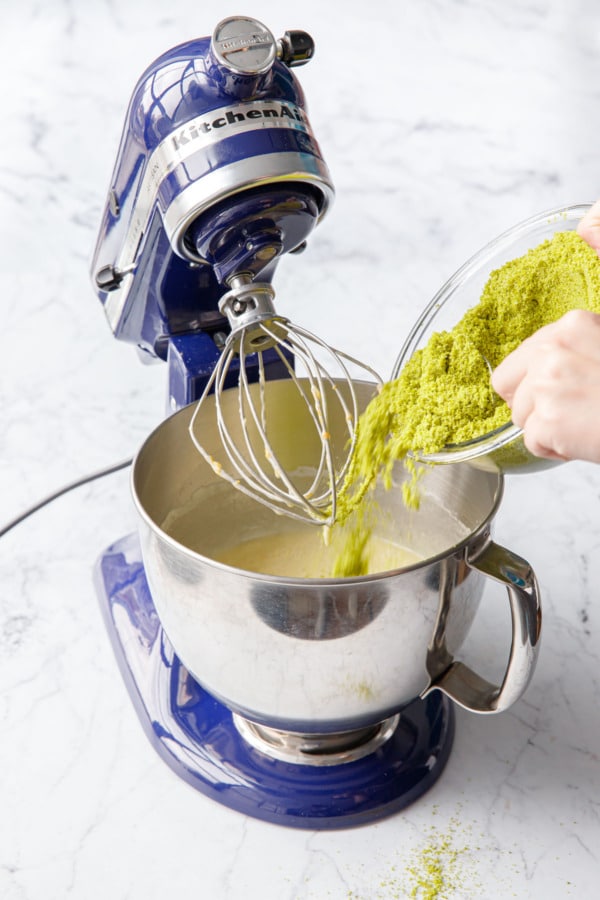 Pouring sifted almond and pistachio flours into mixing bowl with whipped egg mixture.