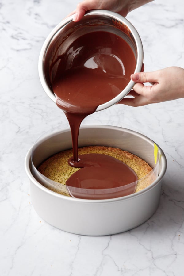 Pouring chocolate ganache onto top of baked cake wrapped in acetate.