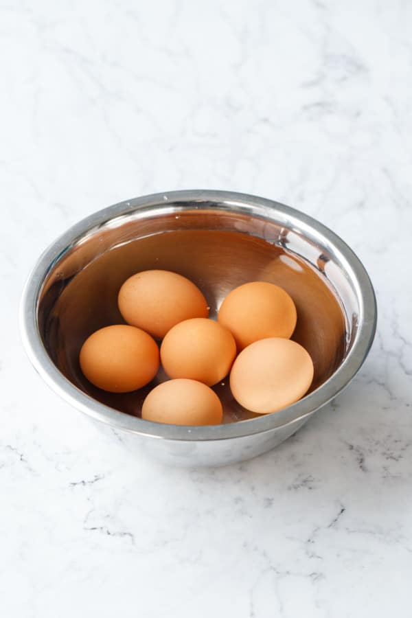 Six brown eggs sitting in a bowl of water on a marble background.