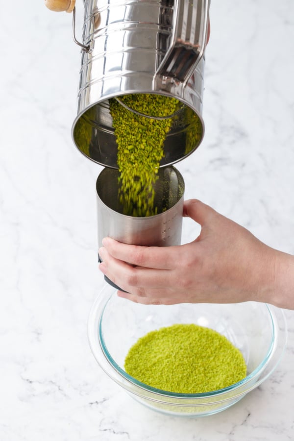 Pouring larger pieces of pistachios back into the canister of a coffee grinder to grind again.