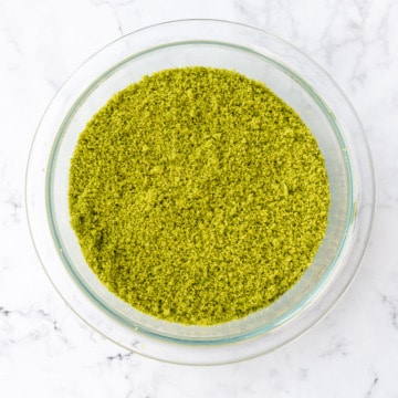 Overhead, bright green Homemade Pistachio Flour in a glass bowl on a marble background.