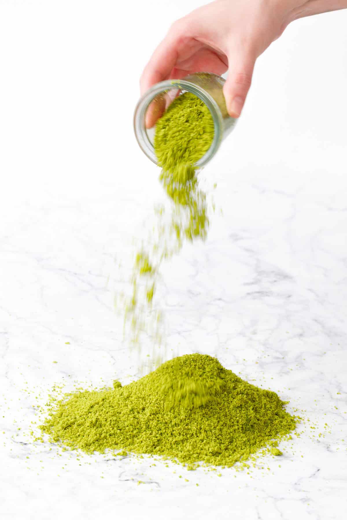 Action shot pouring pistachio flour out of a jar and into a pile on a marble background.