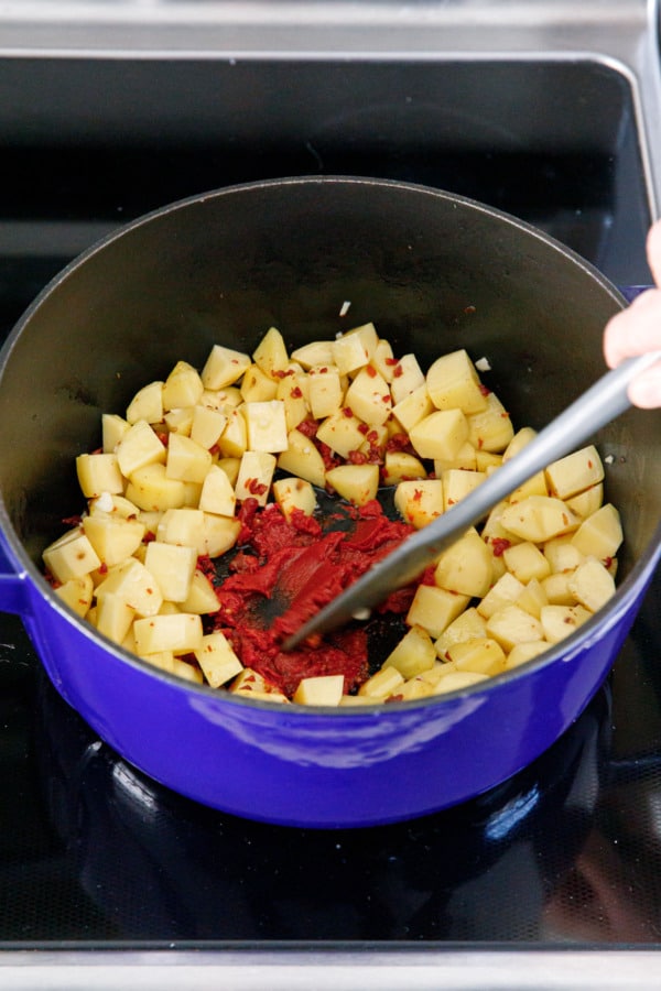 Adding tomato paste to Dutch oven with sautéed potatos and pancetta.