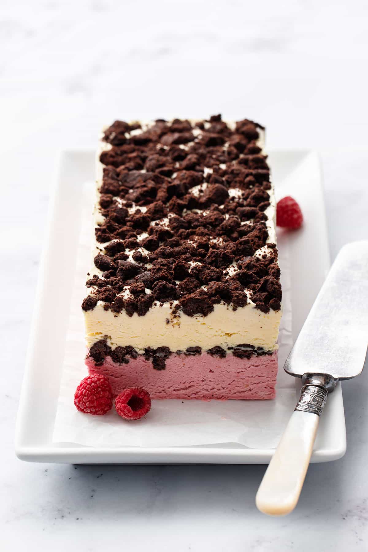 Full loaf of frozen Raspberry & Passionfruit Semifreddo, with visible layers of pink raspberry and pale yellow passionfruit, with Chocolate Crumbs in the middle and on top.