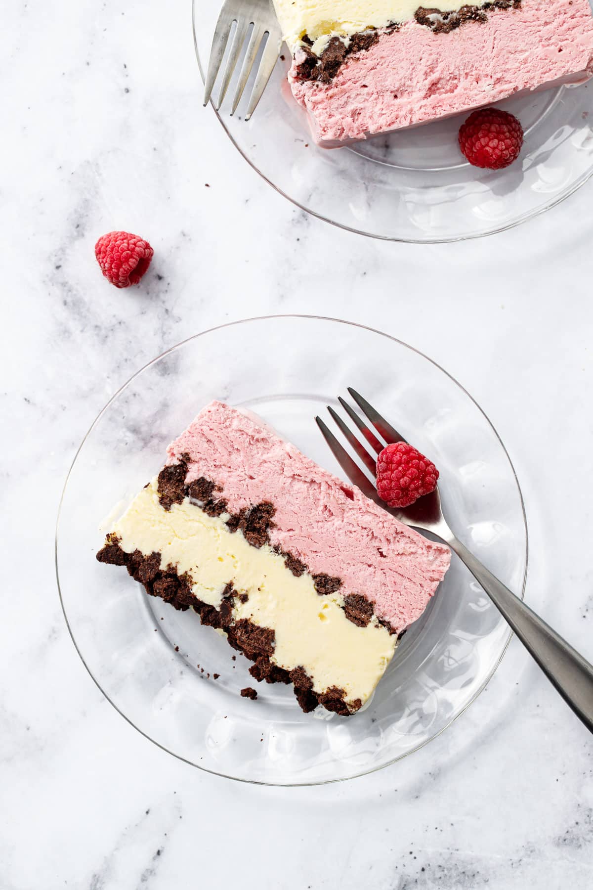 Overhead, slice of Raspberry & Passionfruit Semifreddo with Chocolate Crumbs on a glass plate with fork and frozen raspberries.