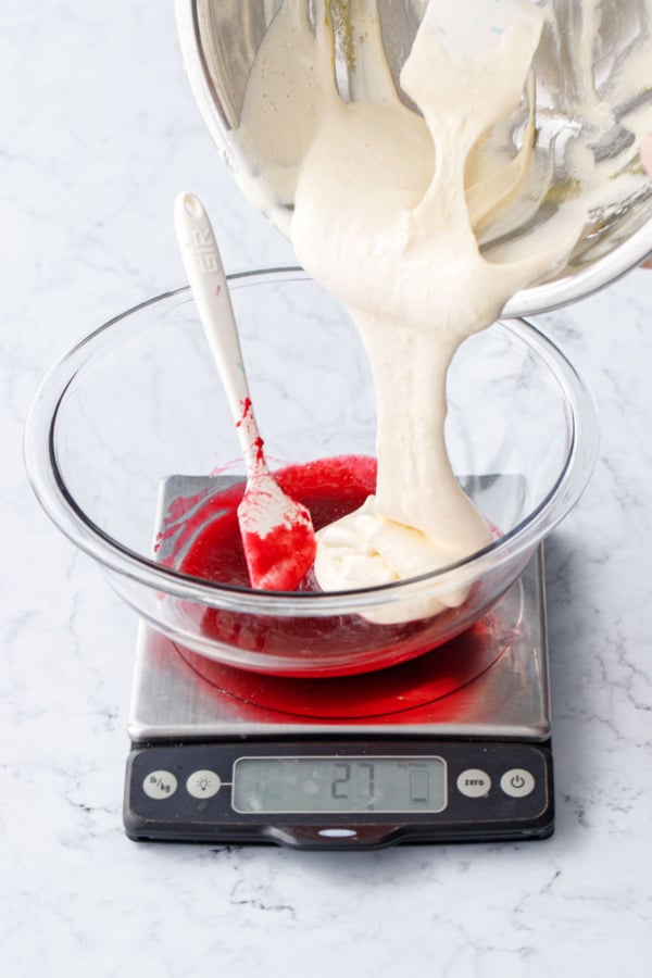 Pouring second half of egg/sugar mixture into a glass mixing bowl with raspberry fruit base.