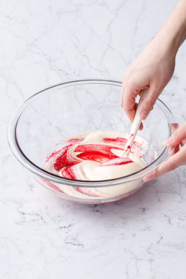 Folding egg/sugar mixture into raspberry puree with a spatula in a glass mixing bowl.