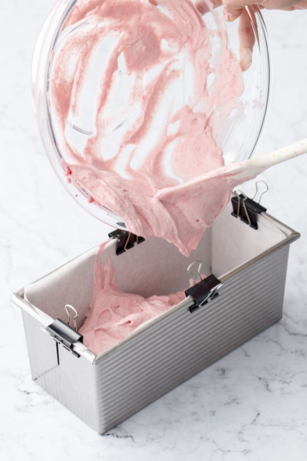 pouring raspberry semifreddo base into parchment-lined loaf pan.