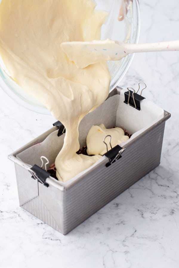 Pouring passionfruit semifreddo on top of frozen raspberry/crumb layer in a parchment-lined loaf pan.