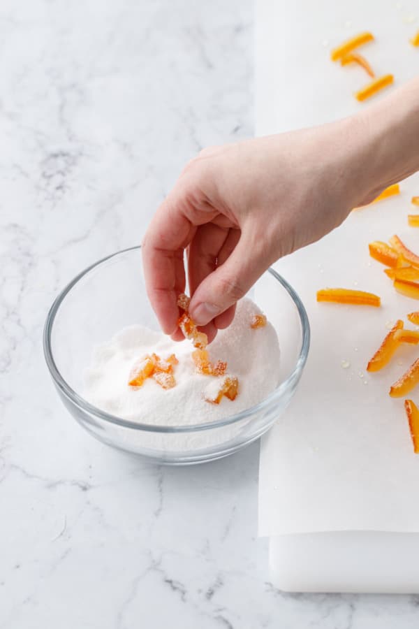 Tossing bits of candied orange peel in granulated sugar to prevent sticking.