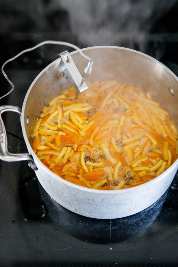 Saucepan with boiling sugar syrup and orange peel.