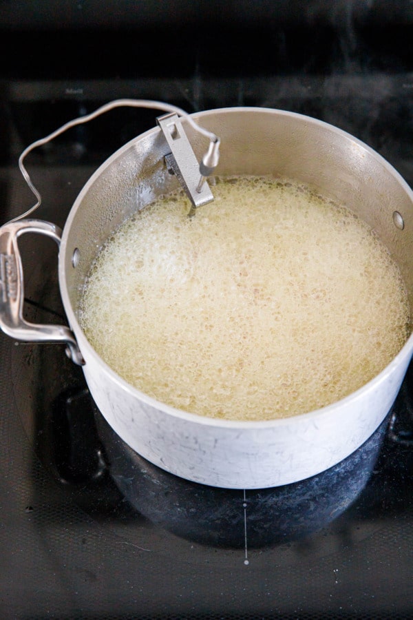 Foamy saucepan with the candied orange peels almost fully covered by bubbles.