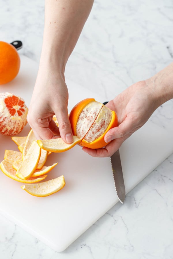 Peeling wedges of orange peel off of the orange flesh to make candied orange peel.