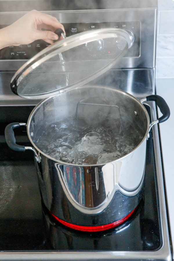 Lifting the lid off the water bath to show the water at a full rolling boil.